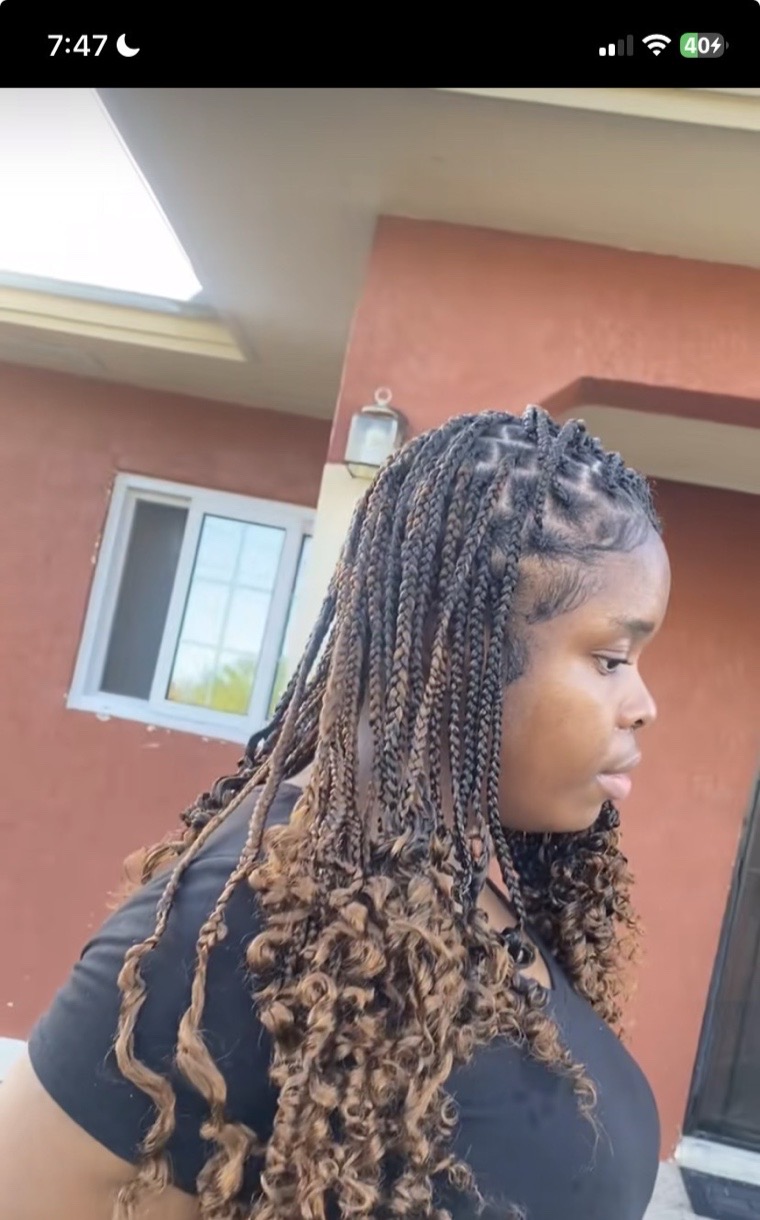 Honey-toned boho knotless braids with curly ends, photographed outdoors.