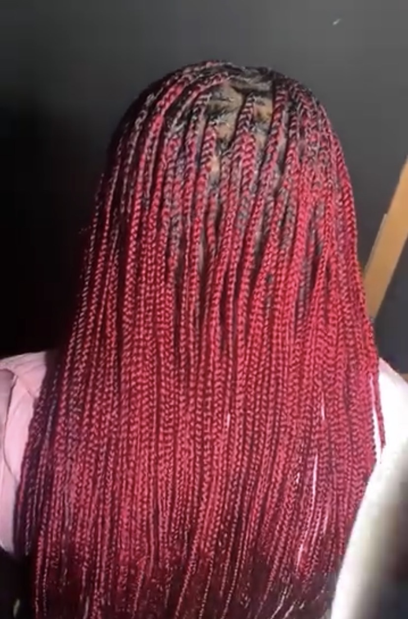 Long knotless braids in a deep red, braided to hip length by Victory Beauty.